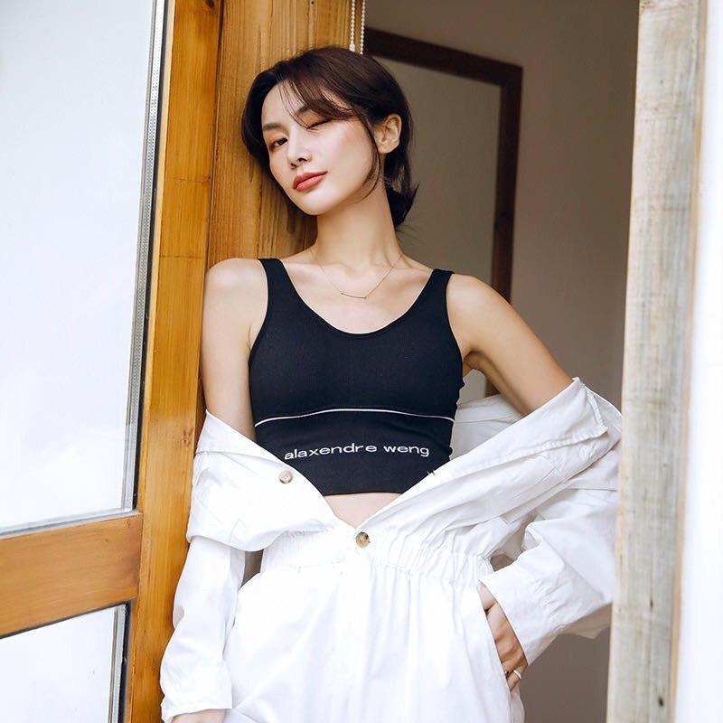 A woman wearing a black sports bra with the brand name visible, paired with a white shirt that is open at the front.